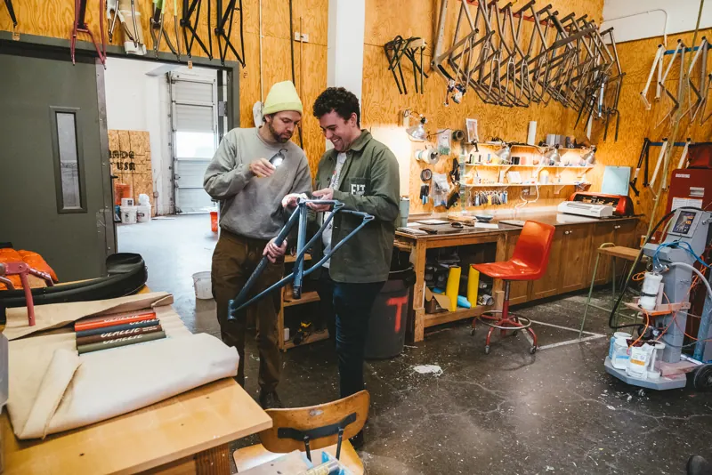 Two people talking over a frame at the shop bench